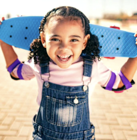 Petite fille souriante avec une planche de skateboard sur les épaules